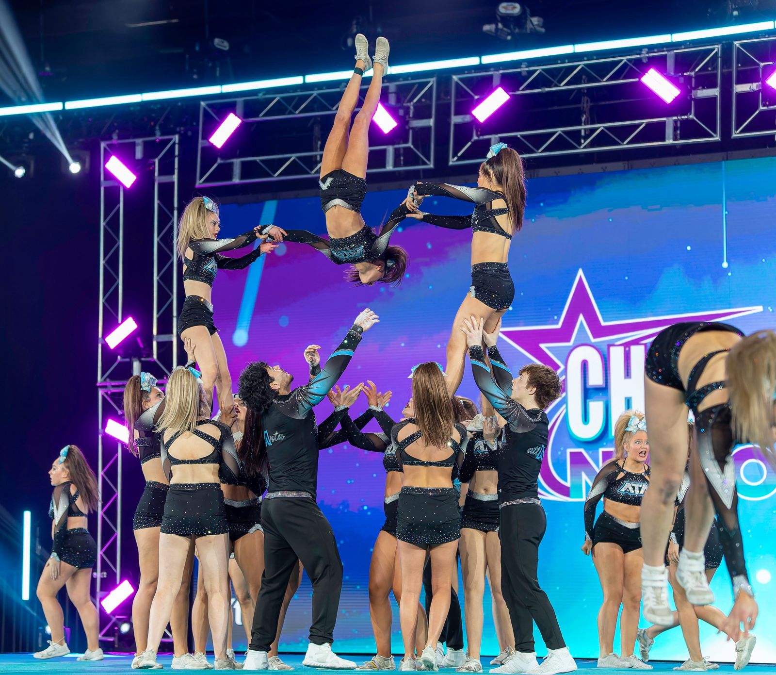 A cheer team holding a pyramid with a flyer flipping between two stunts